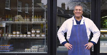 Male baker with blue pinstriped apron standing in front of bakery