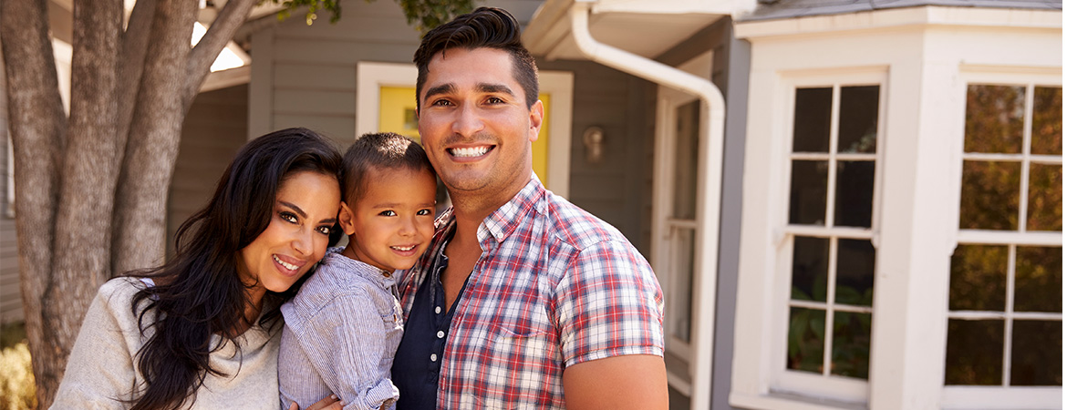 Parents and child smiling in front of their home