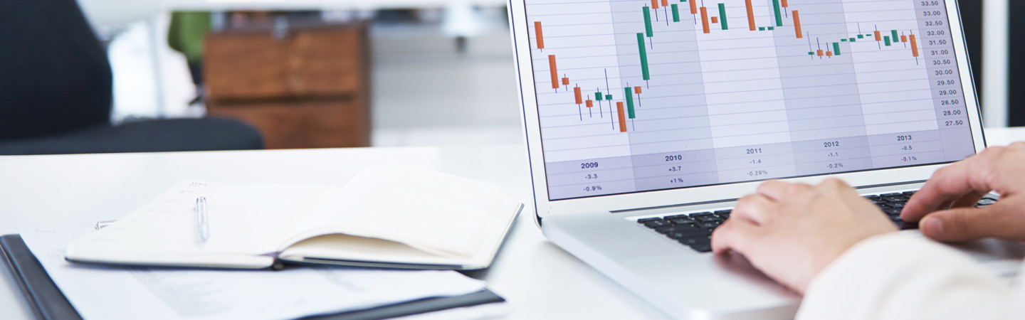 Hands typing on laptop displaying a candlestick chart