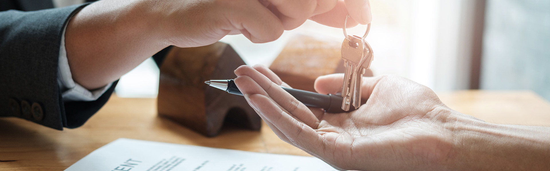 Person handing the keys to a new home to the buyer with a mortgage loan contract and pen in the background