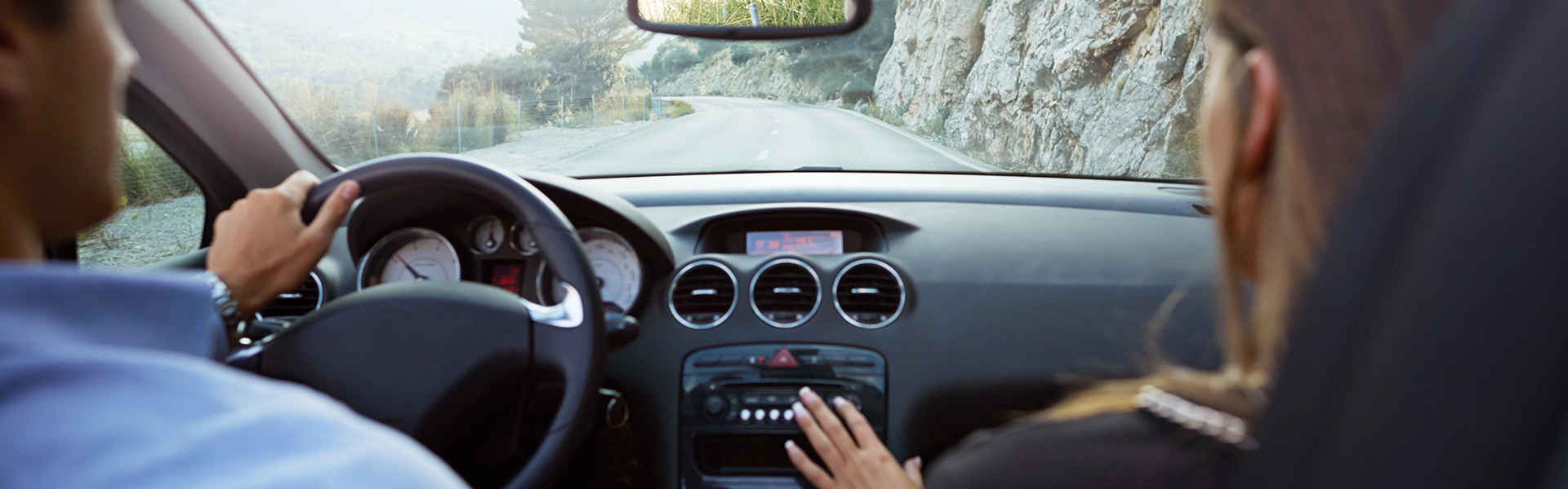 Driver and passenger in vehicle with dashboard and road visible ahead