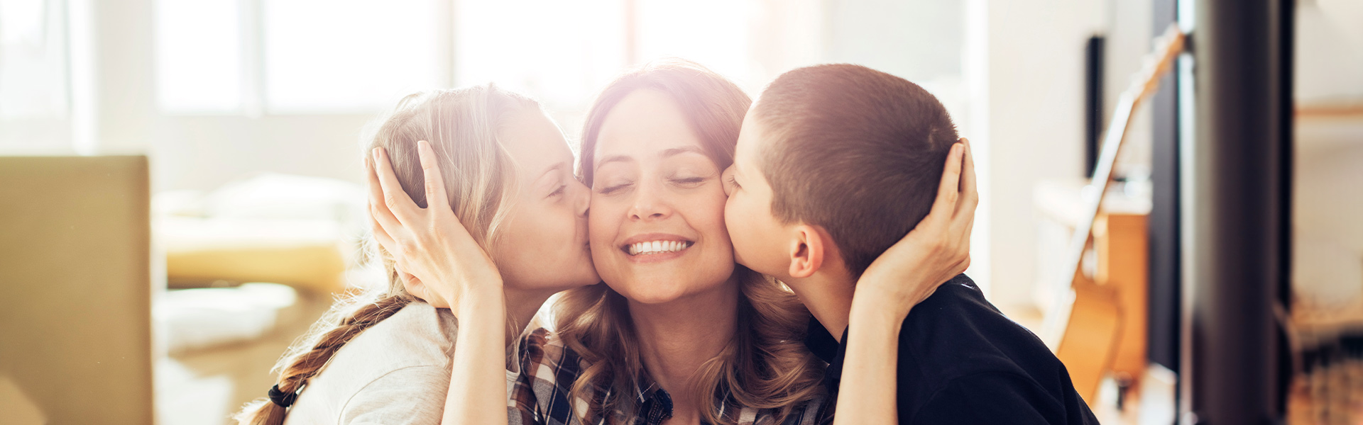 Two young children kissing their mother