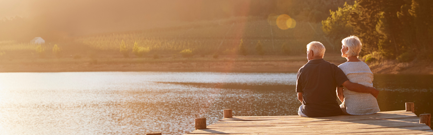 Elderly couple sitting on lake pier looking at view