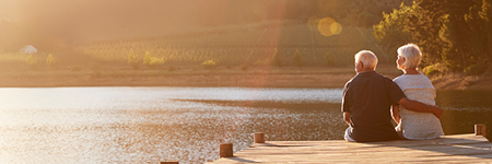 Elderly couple sitting on lake pier looking at view