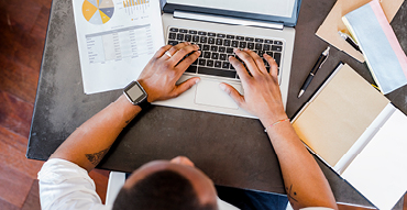 Person using laptop with document showing a financial statement next to them