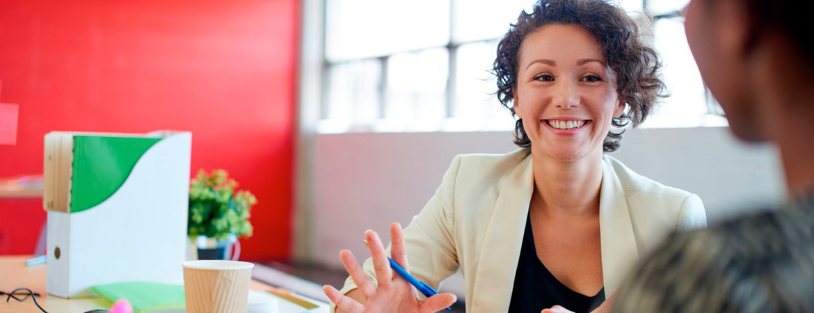 Female relator talking with client in modern office with bright red wall in background.